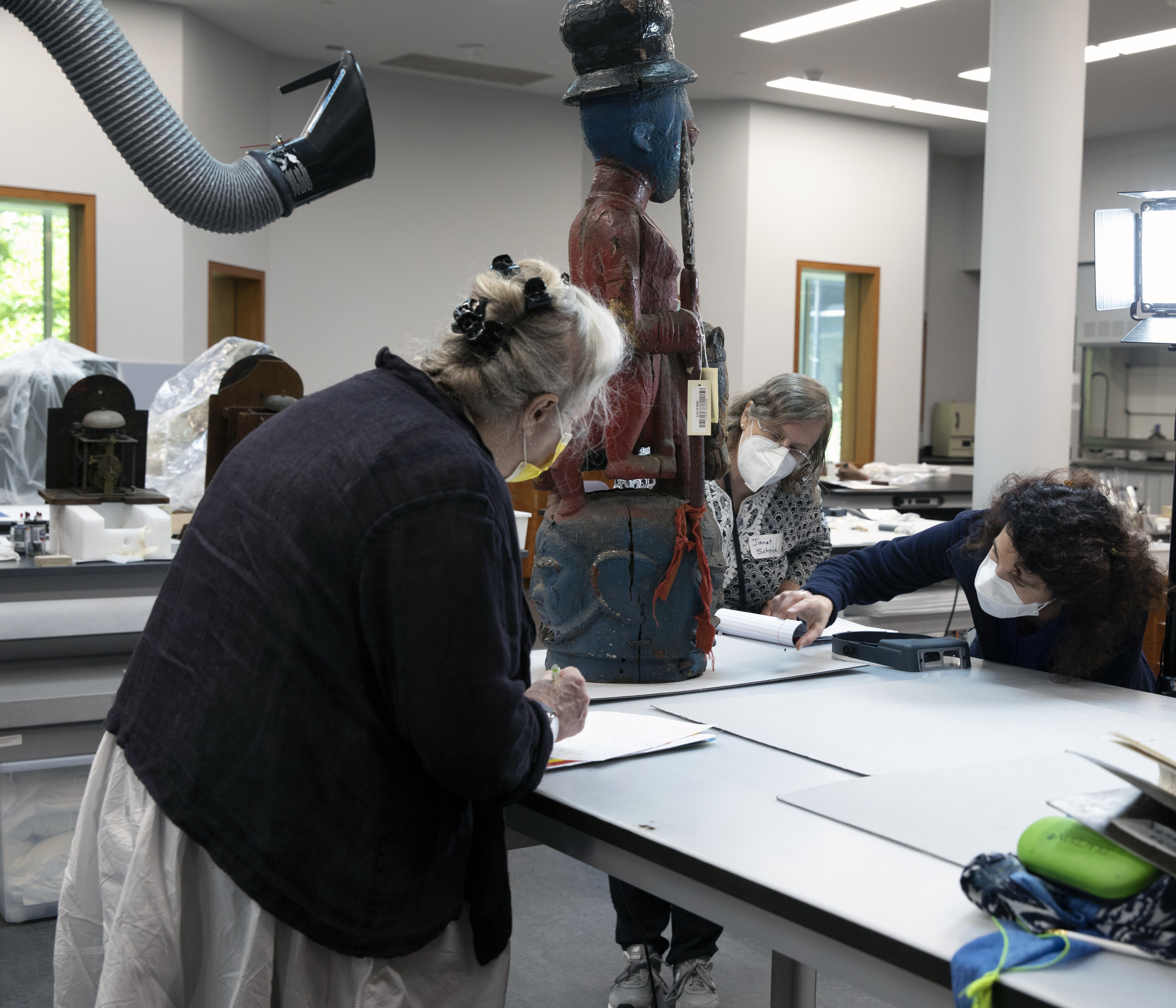 Interior view of Yale’s IPCH with three STITAH participants examining a standing carved wood African figural sculpture on a table.